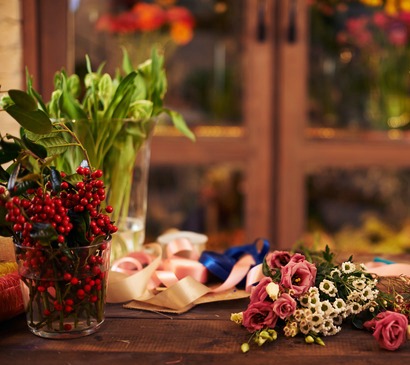 Flowers, berries and decorative ribbons on workplace of florist